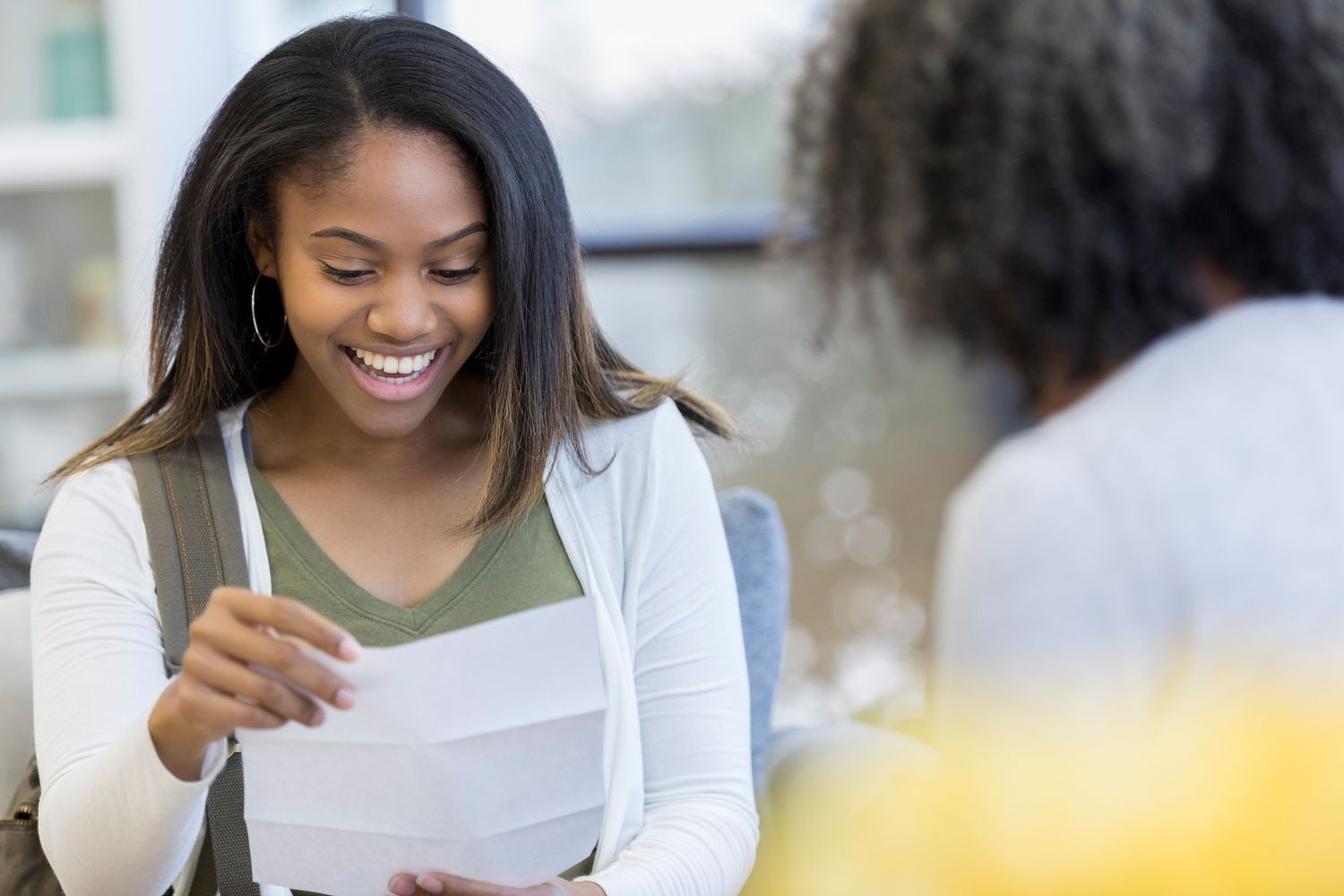 Woman smiling while reading a letter indoors.