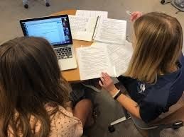 Two people studying with a laptop and papers on a table.